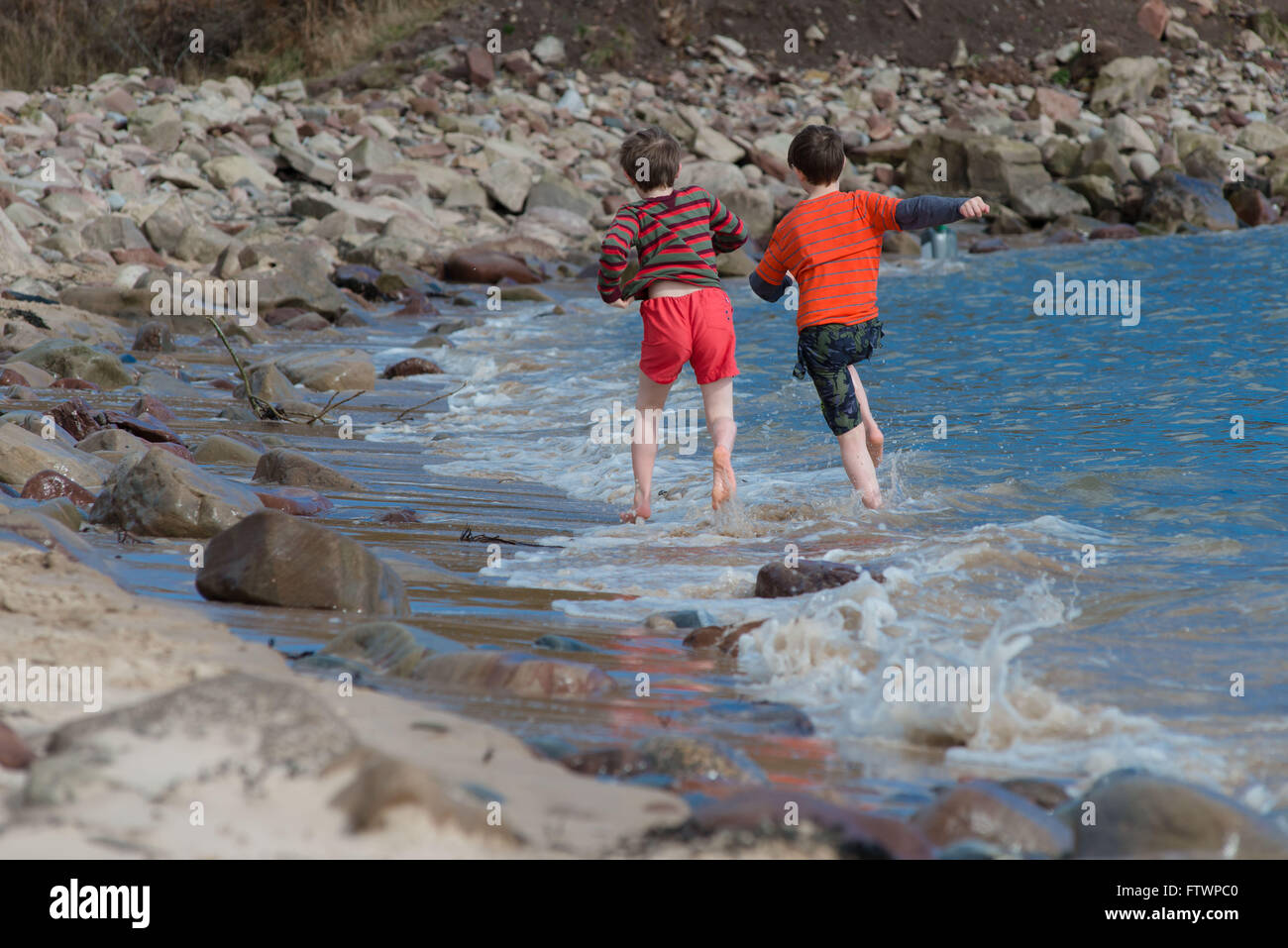 Jungs spielen im Meer in den schottischen Highlands NIgg im Frühjahr mit Badehose Stockfoto