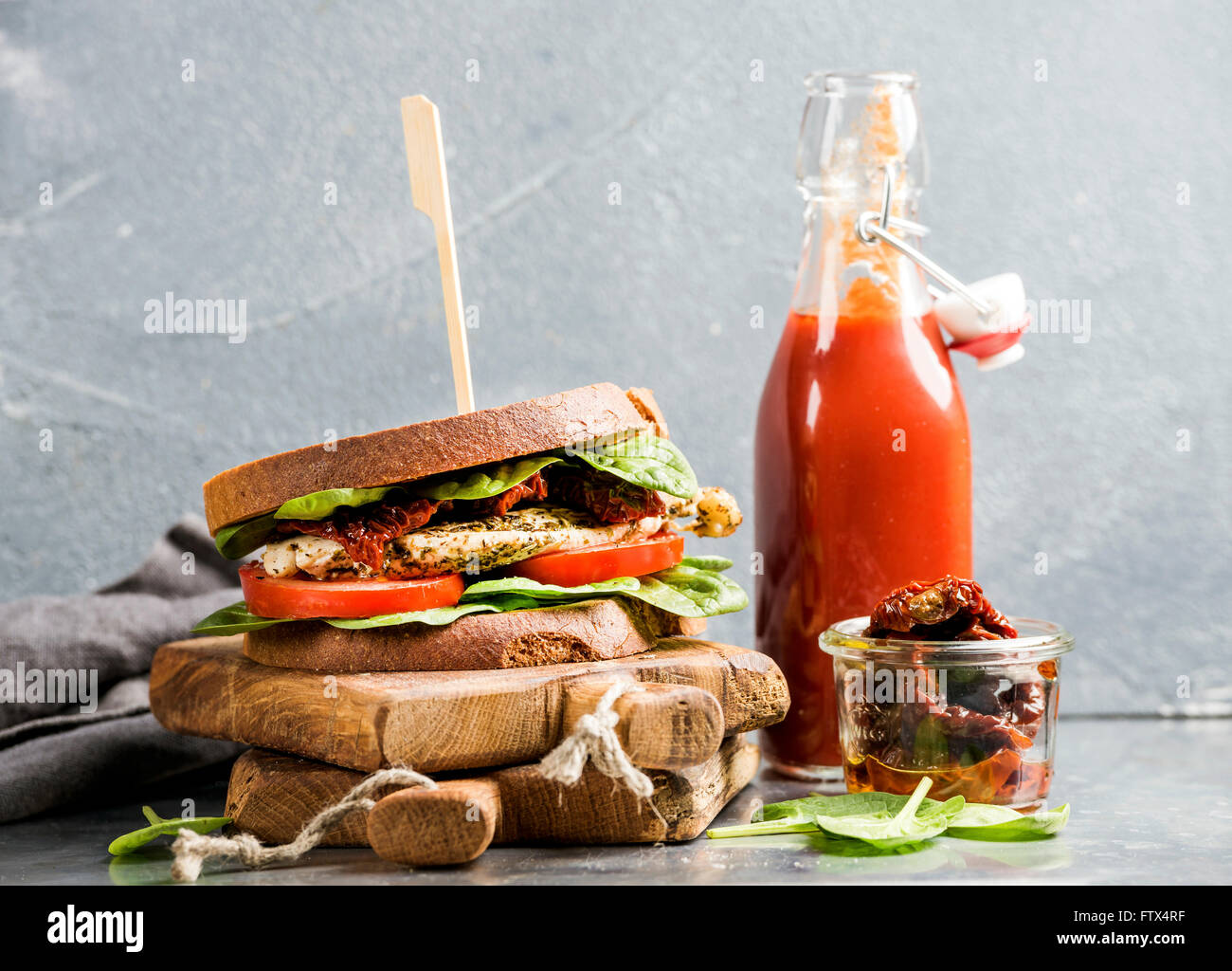 Huhn, getrockneten Tomaten und Spinat Sandwich mit pikanter Sauce auf rustikalem Holzbrett über grauem Beton strukturiertem Hintergrund, s Stockfoto