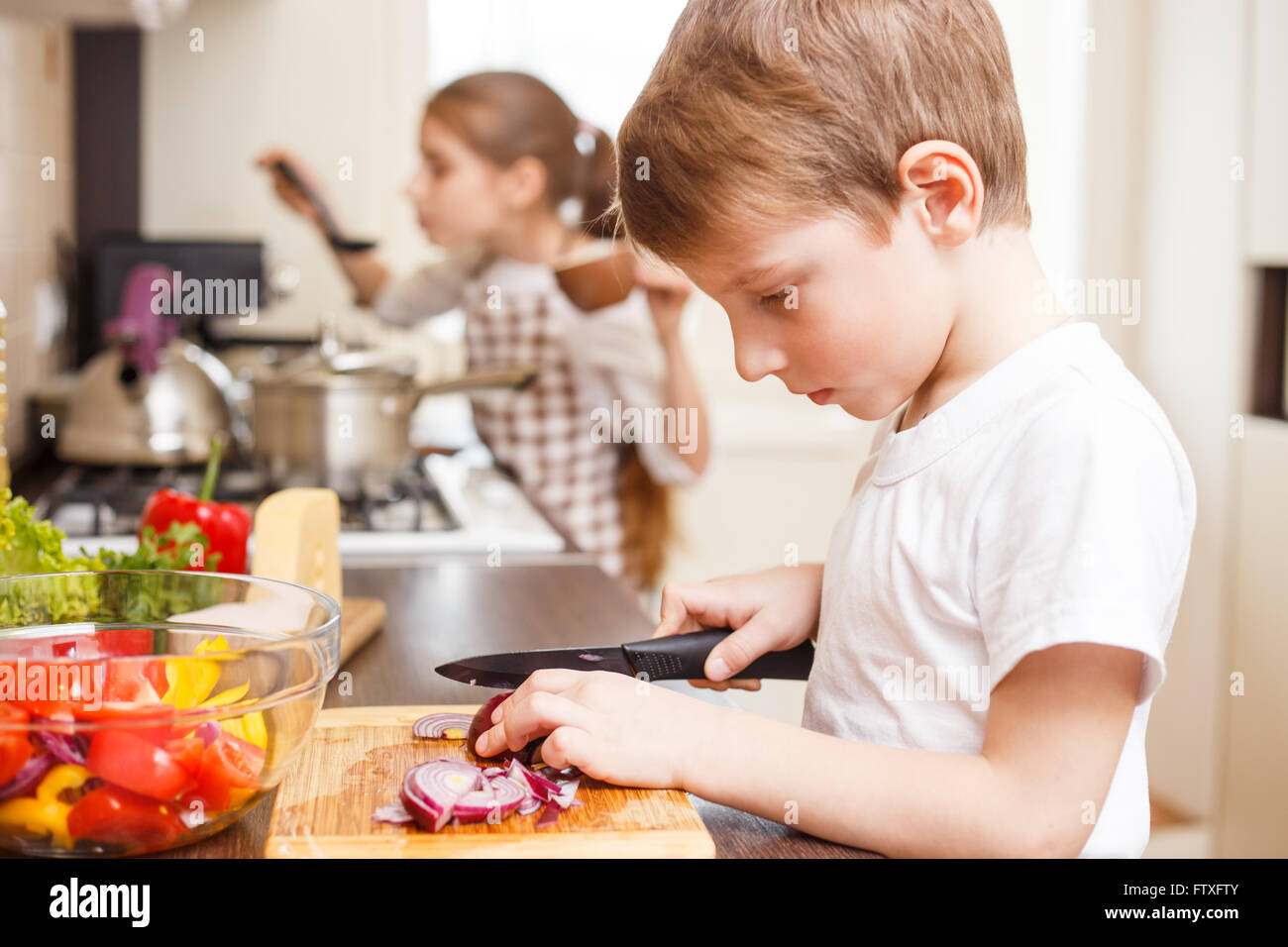 Kleiner Junge und seine Schwester in der Küche. Kleiner Junge schneiden Zwiebel Salat. Stockfoto