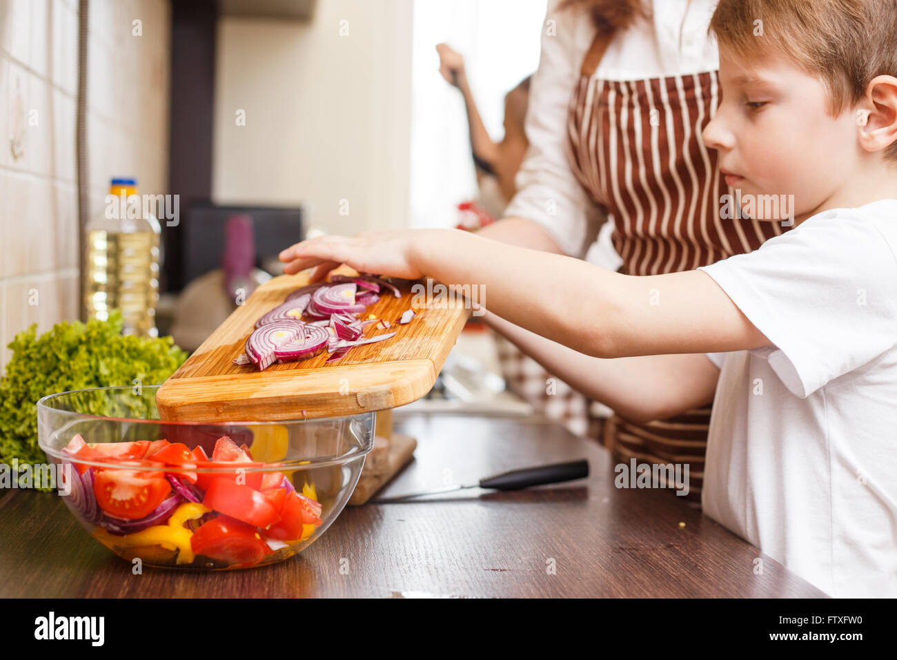 Familie kochen Hintergrund. Kleiner Junge mit schneiden Zwiebel Salat in der Küche seiner Mutter helfen Stockfoto