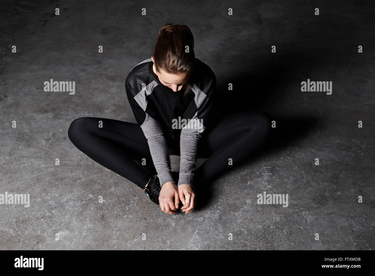 Junge Frau sitzt auf dem Boden in Turnhalle Aufwärmen Stockfoto