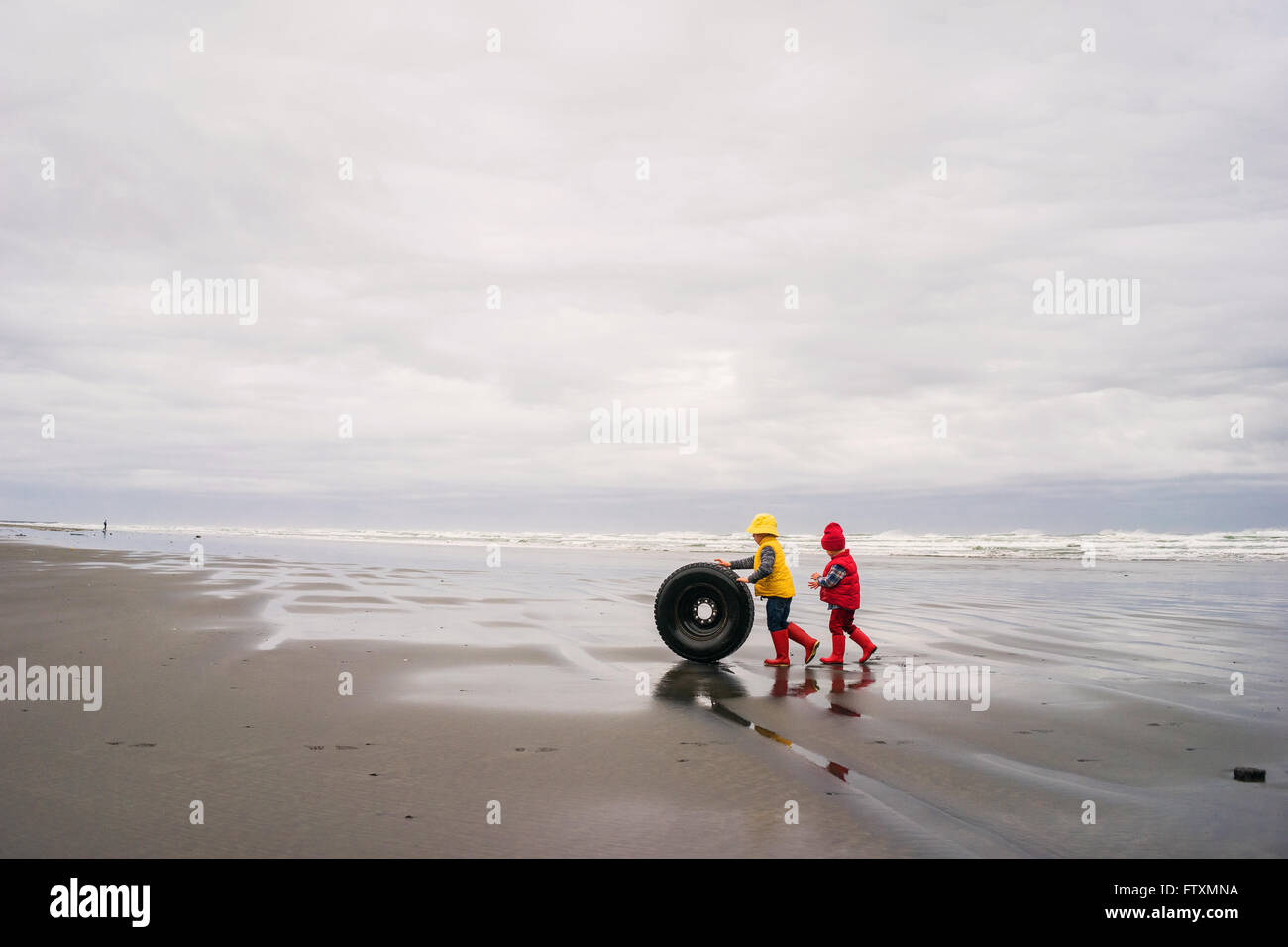 Zwei jungen, die einen verlassenen Reifen aus dem Meer an den Strand Rollen Stockfoto