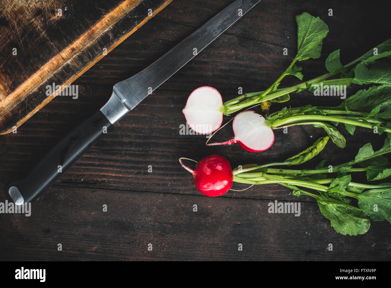 Radieschen mit einem Messer und hacken Brett auf einem Holztisch Stockfoto