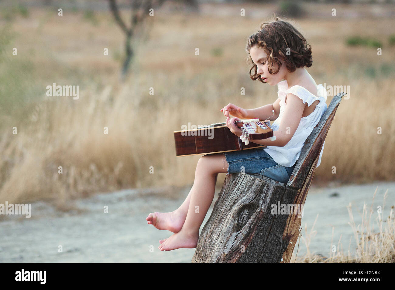 Mädchen sitzen in einem Feld, Gitarre zu spielen Stockfoto