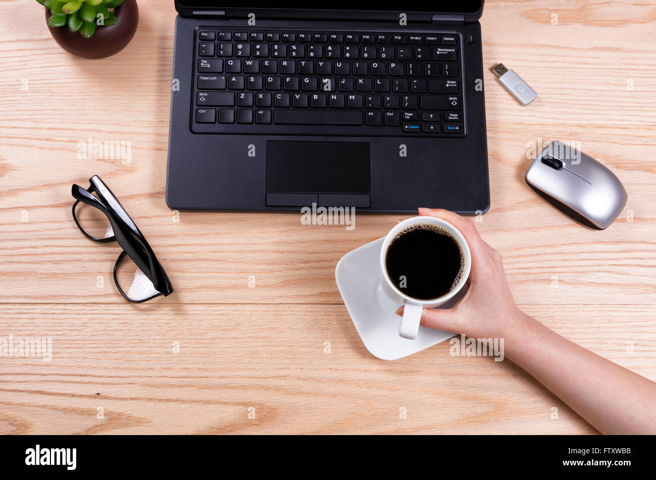 Draufsicht auf der Hand, die Kaffeetasse mit Laptop, Babypflanze, Maus, USB-Stick und Lesebrille auf Desktop. Stockfoto