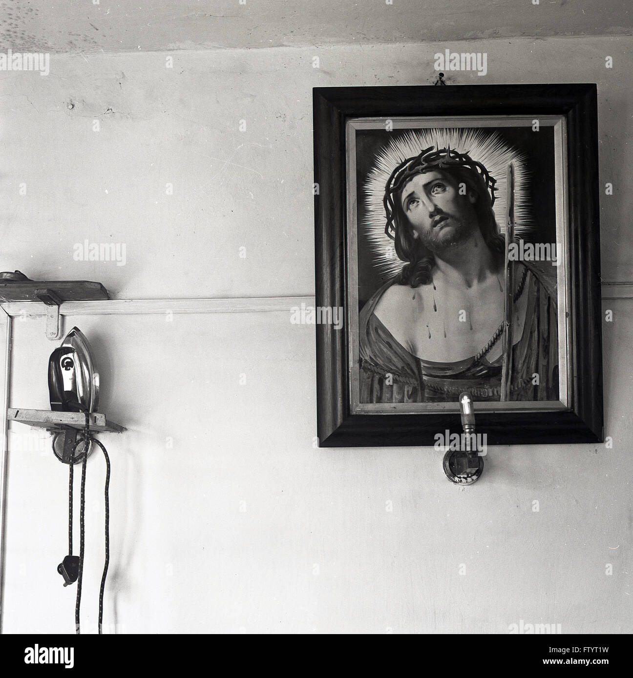 der 1950er Jahre, Historienmalerei Jesu Christi mit einem Ring aus Licht oder Halo um sein Gesicht an Wand, mit Licht unter und Eisen an Wand. Stockfoto