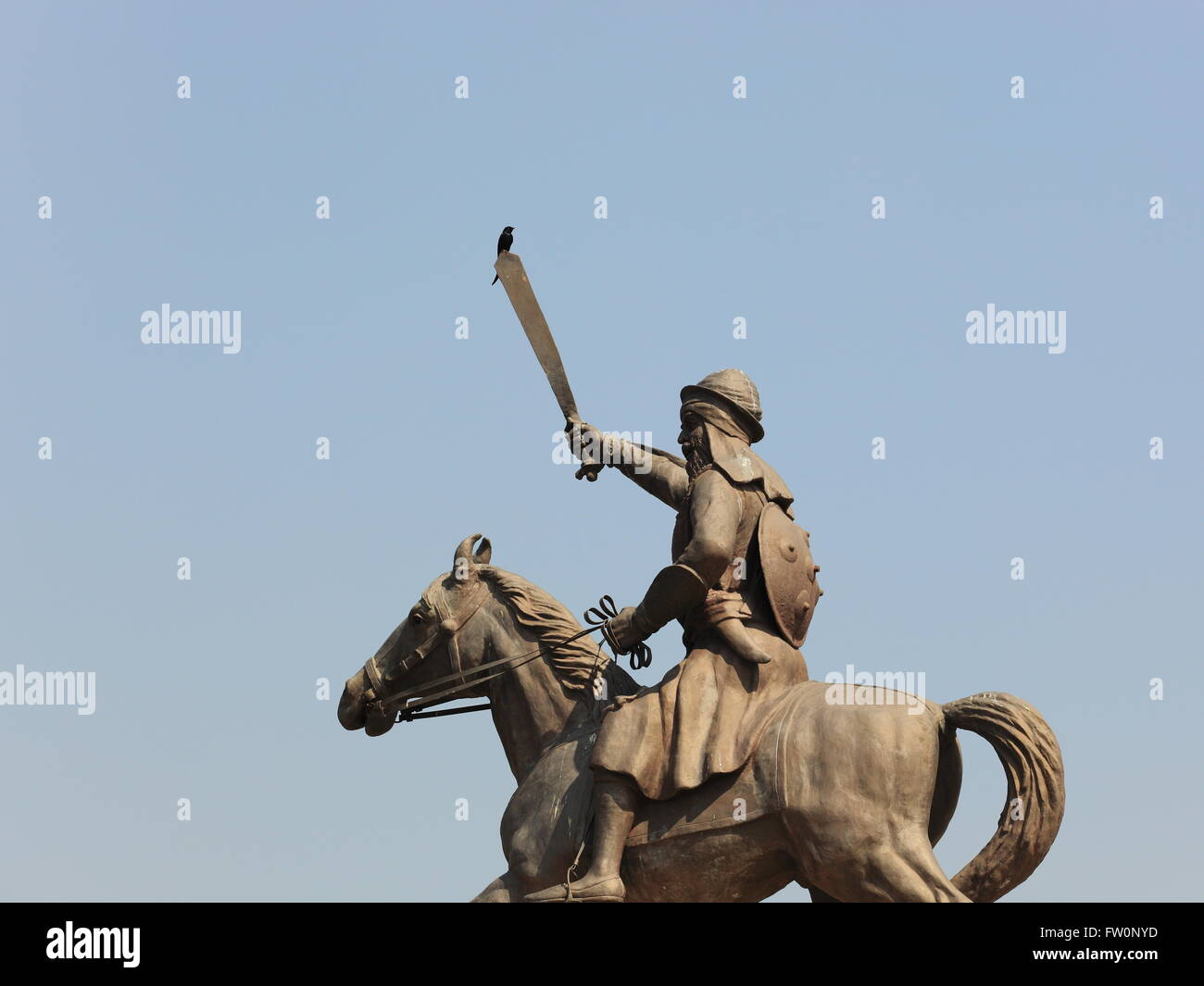 Ein schwarzer Drongo hockt auf das Schwert einer montierten Sikh Krieger-Statue an der Baba Banda Singh Bahadur-Gedenkstätte in Punjab, Indien. Stockfoto