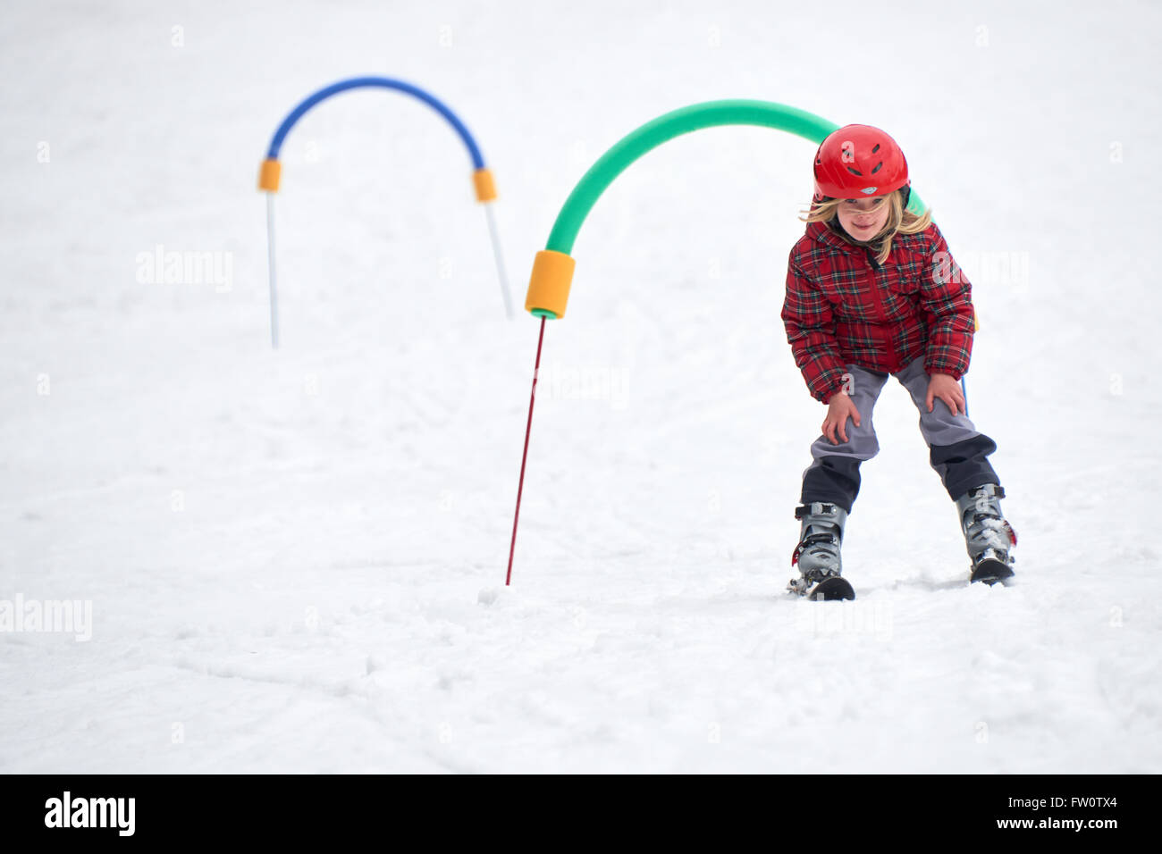 Kind beim Skifahren in den Bergen. Mädchen mit Schutzhelm Skifahren lernen in der Schule. Wintersport für Familien mit kleinen Kindern. Stockfoto