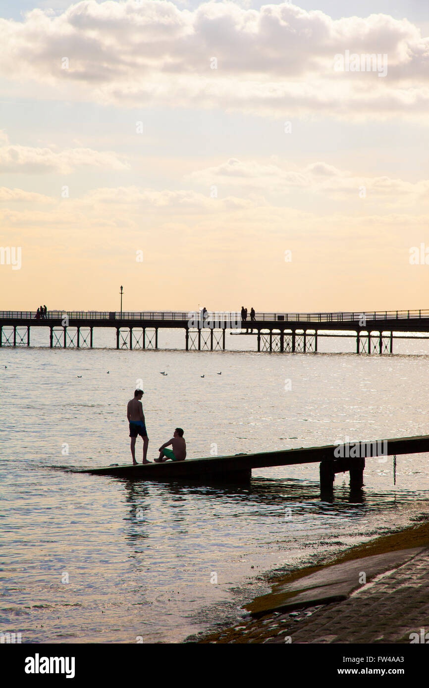 Zwei Jungs sitzen am Ende eines Piers mit einer anderen Pier im Hintergrund (Southend-on-Sea, Essex, UK) Stockfoto