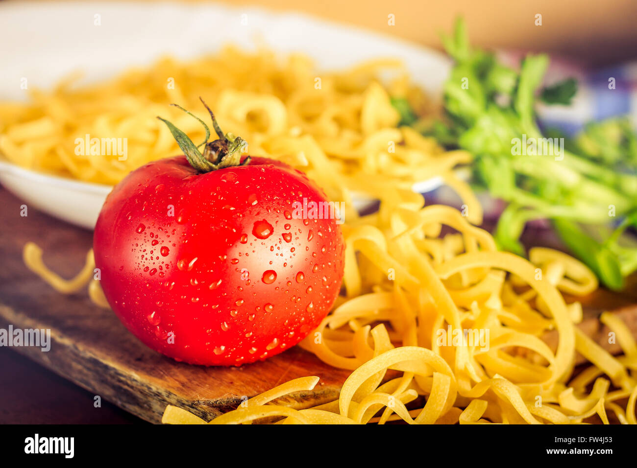 Frische Tomaten neben Teller voll mit rohen ungekochten Nudeln Stockfoto