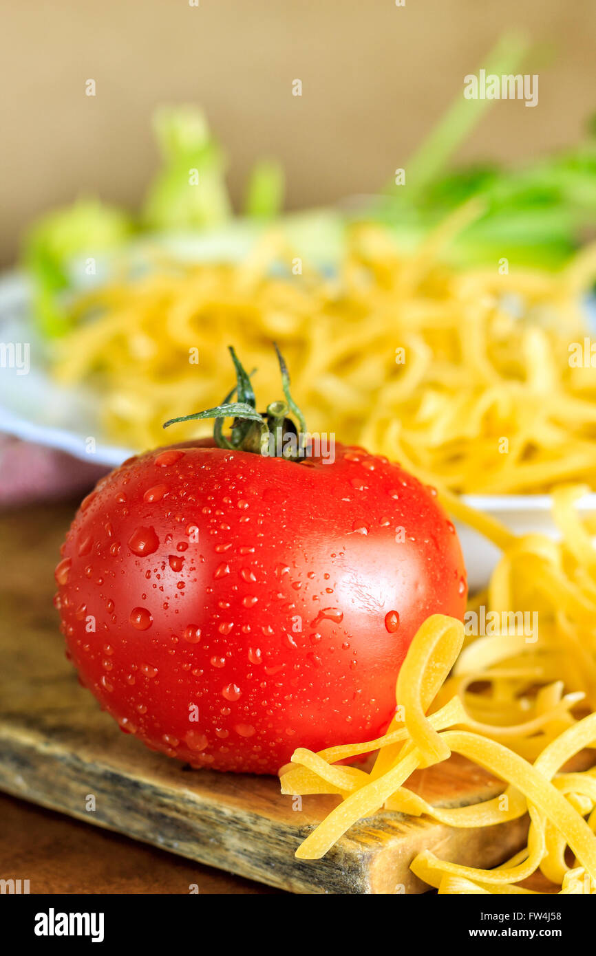 Frische Tomaten neben Teller voll mit rohen ungekochten Nudeln Stockfoto