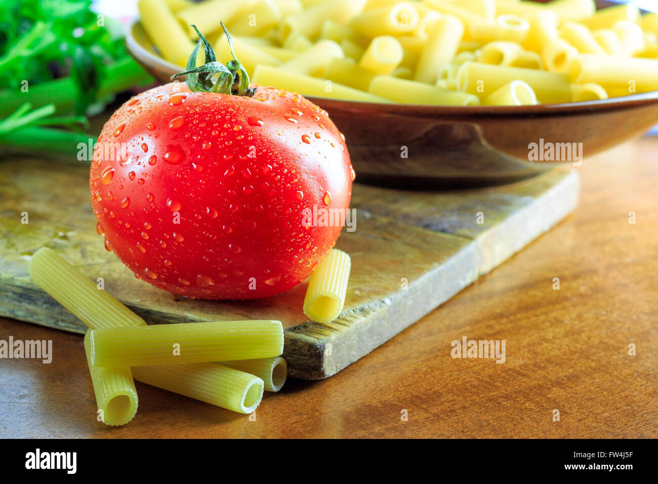 Frische Tomaten neben Teller voller rohe ungekochte Teigwaren. Textfreiraum Stockfoto