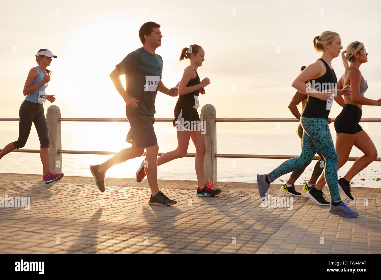 Gruppe von Jugendlichen in einem Rennen zu konkurrieren. Junge Männer und Frauen laufen direkt am Meer bei Sonnenuntergang die promenade. Stockfoto