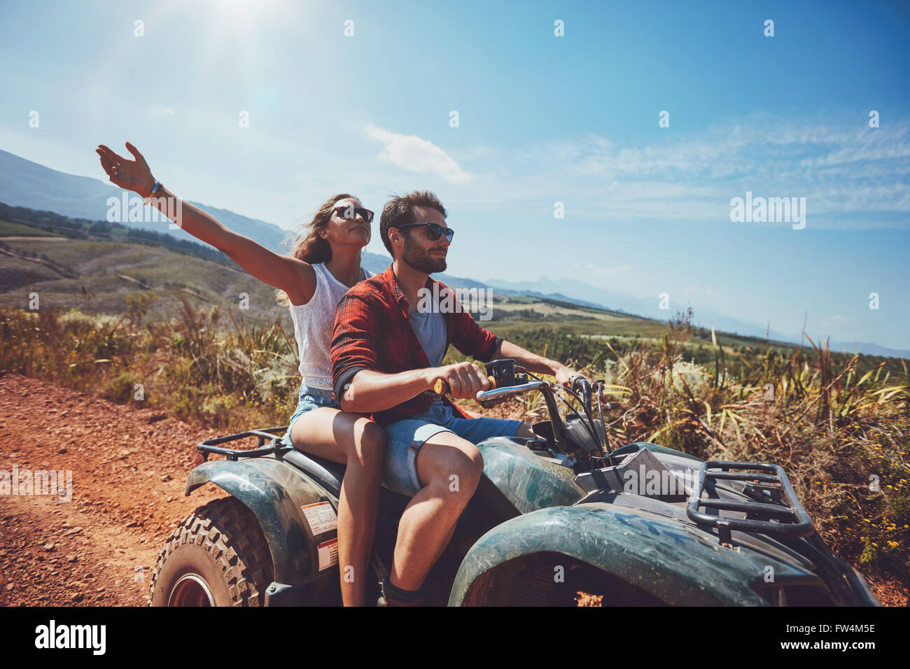 Glückliches junges Paar in der Natur auf einem Quad-Bike. Junger Mann und Frau genießen ein Quad-Bike fahren in Landschaft. Fahren Mann und Frau Stockfoto