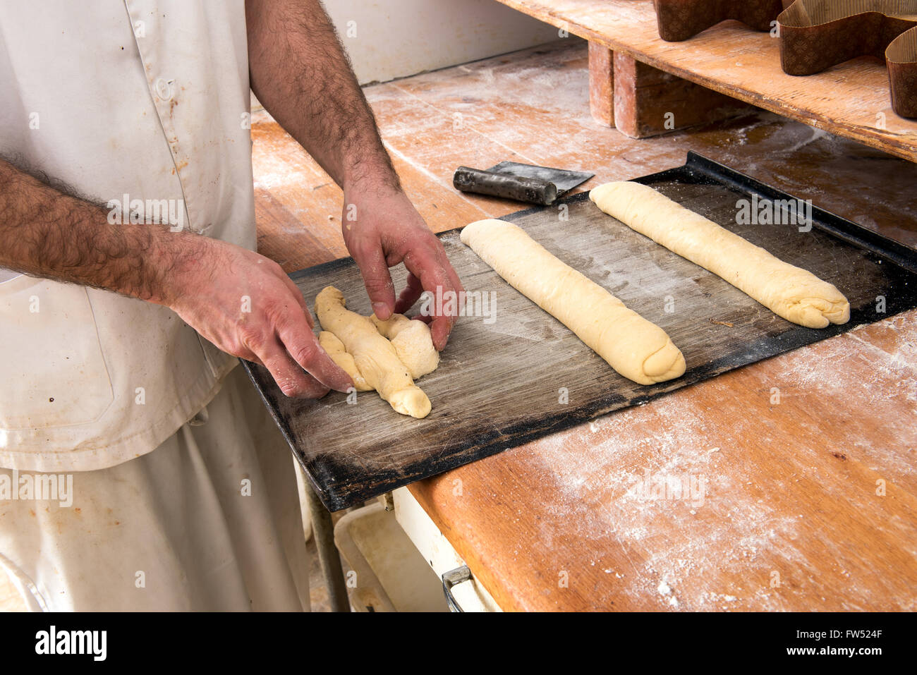 Bäcker arbeiten mit rohen Teig bildet es in langen Rollen und Formen, Nahaufnahme von seinen Händen und einem langen Holztisch Stockfoto