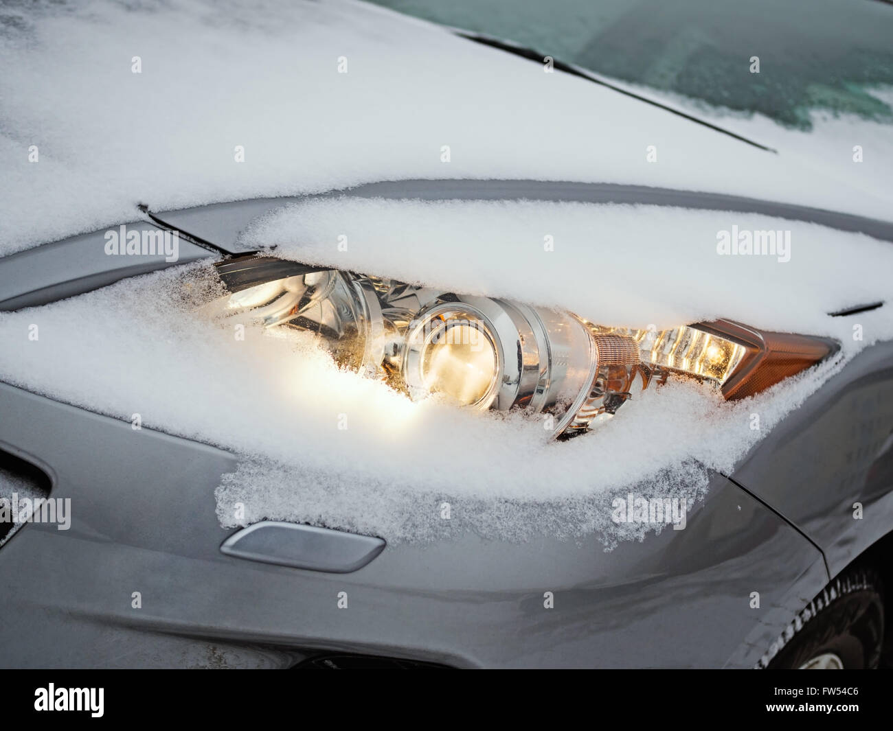Leuchtende Scheinwerfer eines Autos mit Schnee bedeckt, wie es während eines Schneesturms gefahren wird Stockfoto