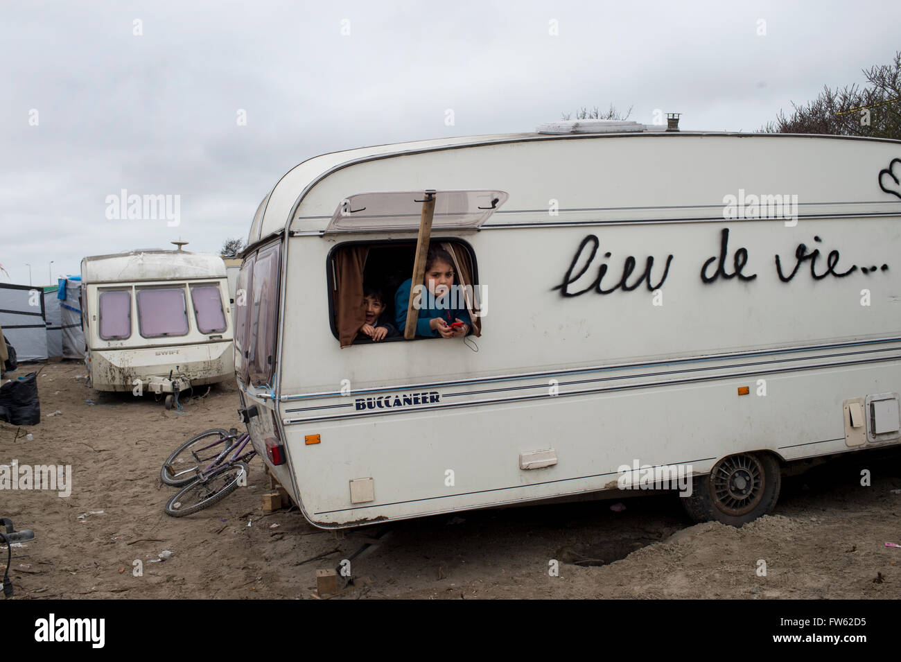 Frankreich, Calais. Flüchtlingslager - die so genannte Dschungel. Zwei junge kurdische irakische Flüchtlingskinder schauen aus einem Wohnwagen-Fenster Stockfoto