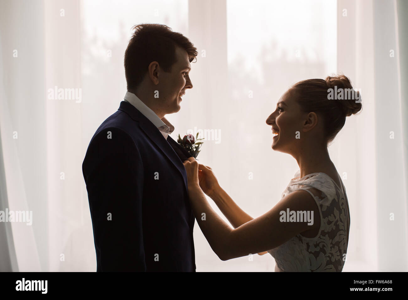 Glücklich Frischvermählten, die Brünette Braut Blume Pins entsprechend der Bräutigam bei der Fenster-Silhouetten von glücklich Stockfoto