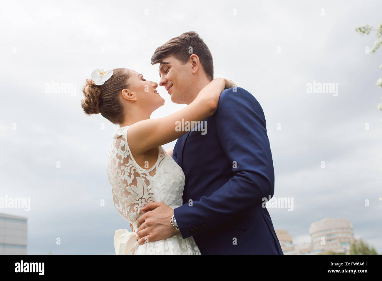 Porträt der jungen glücklich schöne Brautpaar schauen einander, umarmt und Lächeln auf blauen Himmelshintergrund Stockfoto