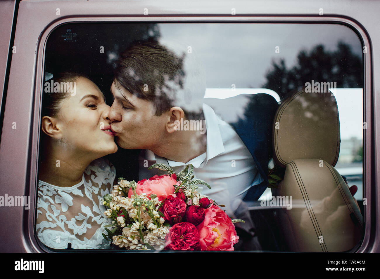 Der Bräutigam küsst die Braut, der Blick durch das Glas des Autos Stockfoto