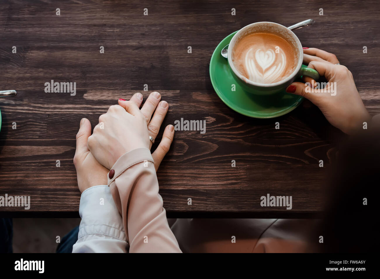 Das Mädchen hält die Hand ihres Mannes, Hände Nahaufnahme Tasse Kaffee und Cappuccino, Ansicht von oben auf einem Holztisch Stockfoto