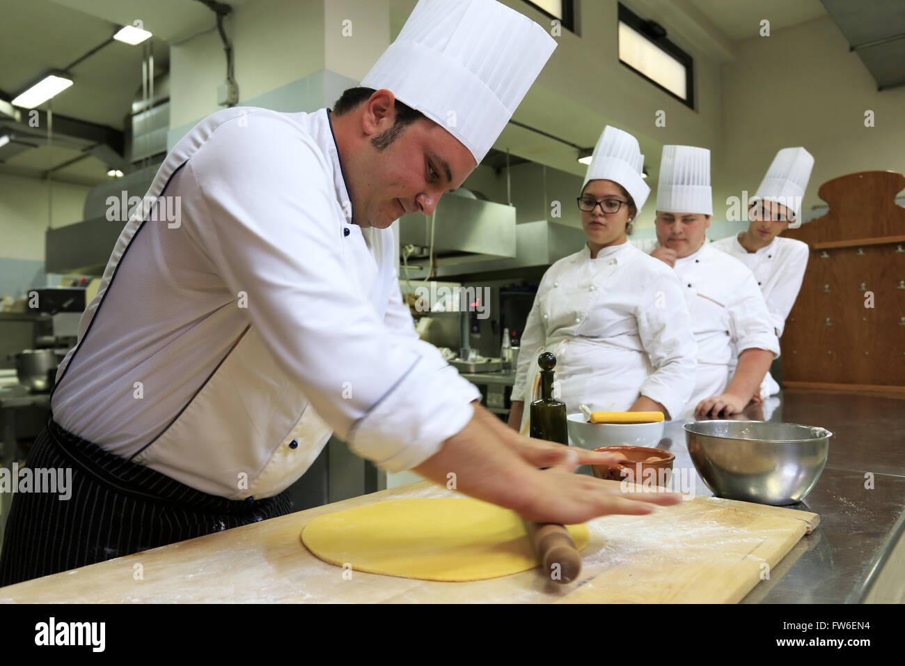 Ein Koch macht frischen Pasta in Küche mit Lehrlingen im Hintergrund, Gubbio, Umbrien, Italien Stockfoto