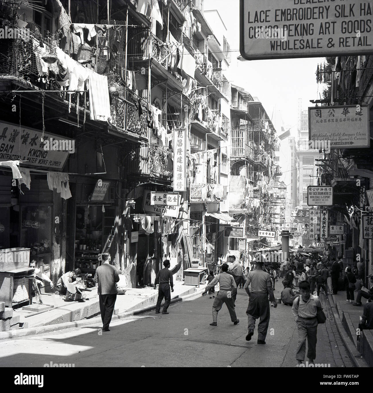 Die 50er Jahre, historisch, tagsüber und ein Blick auf eine Straße in der Altstadt von Hongkong, der die Schichten verschiedener Stockwerke über den Geschäften und Verkäufern im Erdgeschoss zeigt. Stockfoto