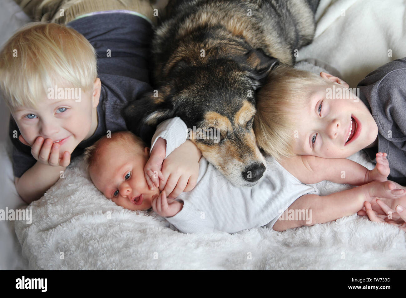 Drei glückliche junge Kinder, darunter ein neugeborenes Mädchen, ein Kleinkind und ihre Big Brother liegen im Bett kuscheln mit den Stockfoto