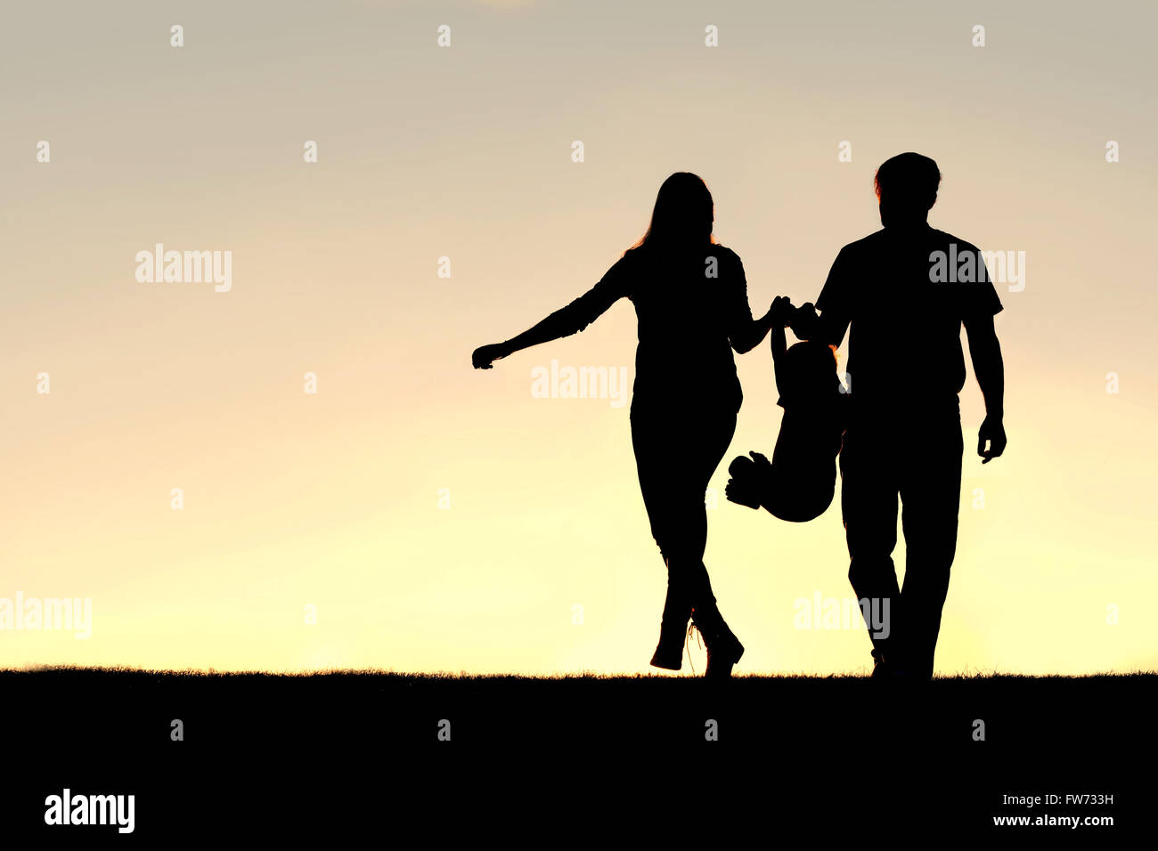 Eine Silhouette einer Familie von drei Menschen, darunter auch Mutter, Vater und Kind sind bei einem Spaziergang außerhalb am Herumspielen Stockfoto