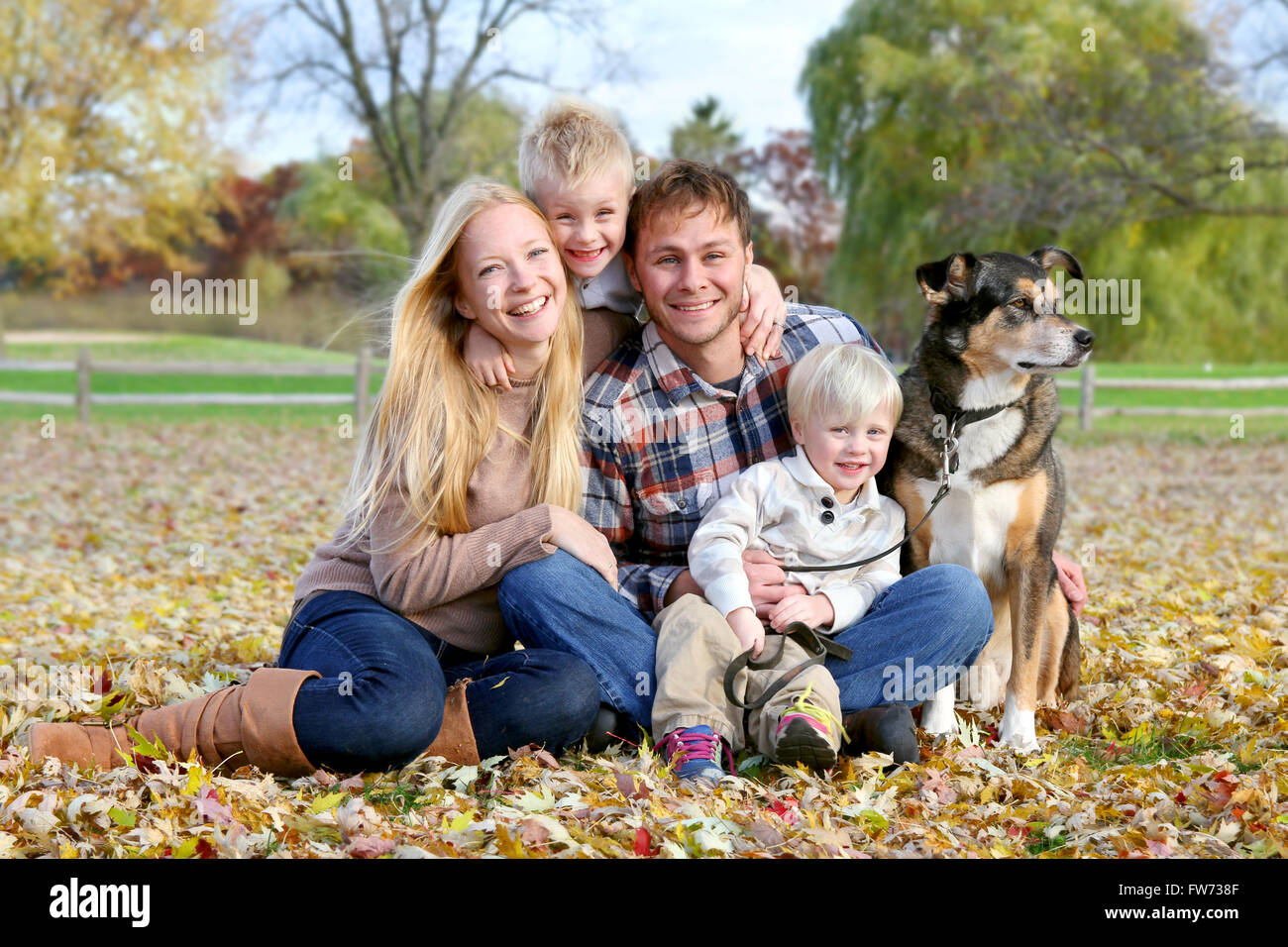 Eine glückliche Familie von vier Personen, darunter Mutter, Vater, Kind und Kleinkind Bruder sitzen draußen im Laub Stockfoto