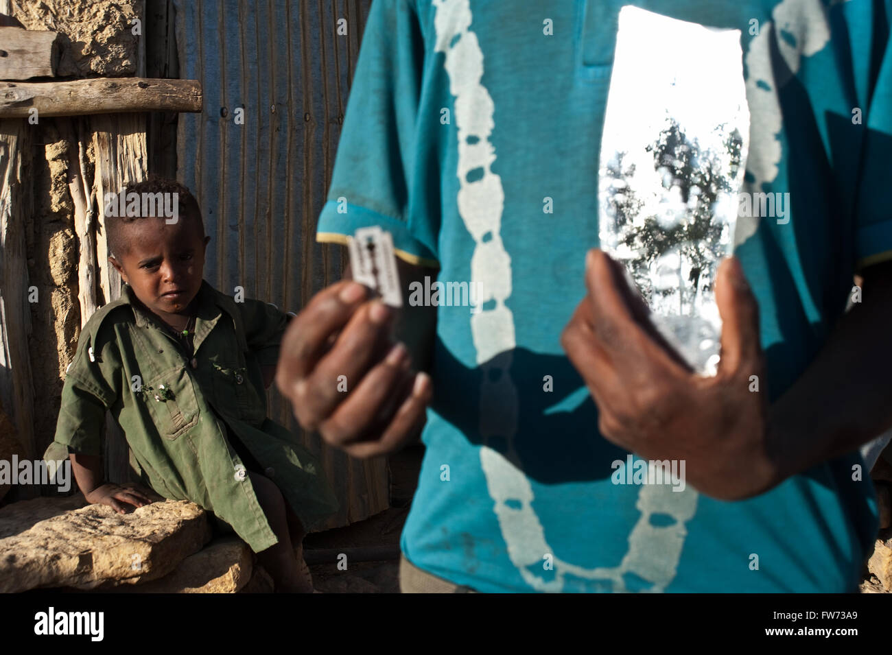 Zeigt ein Agow Man ein Messer und einen Spiegel, mit denen die Kinder Haare (Äthiopien) rasieren Stockfoto