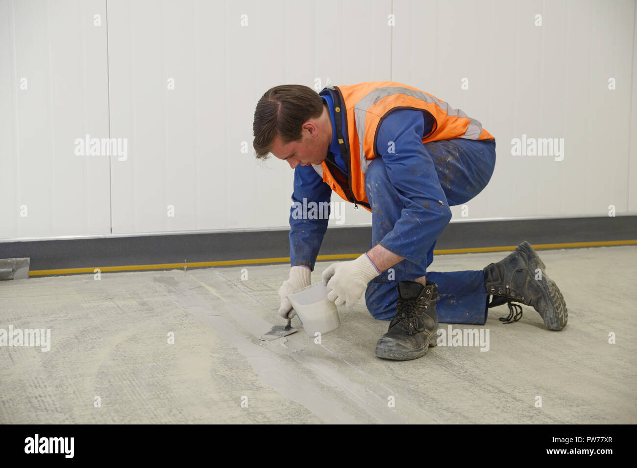 Ein Tradesmans füllt Risse im Boden in einem Industriegebäude, bevor der Epoxy Bodenbelag untergeht Stockfoto