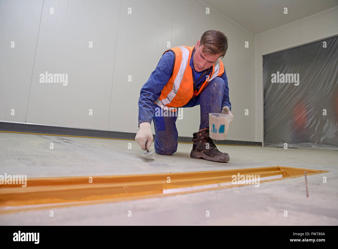 Ein Tradesmans füllt Risse im Boden in einem Industriegebäude, bevor der Epoxy Bodenbelag untergeht Stockfoto