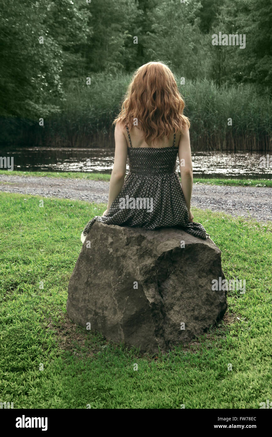 Rückansicht einer jungen Frau im gepunkteten Kleid sitzt auf einem Felsen Stockfoto