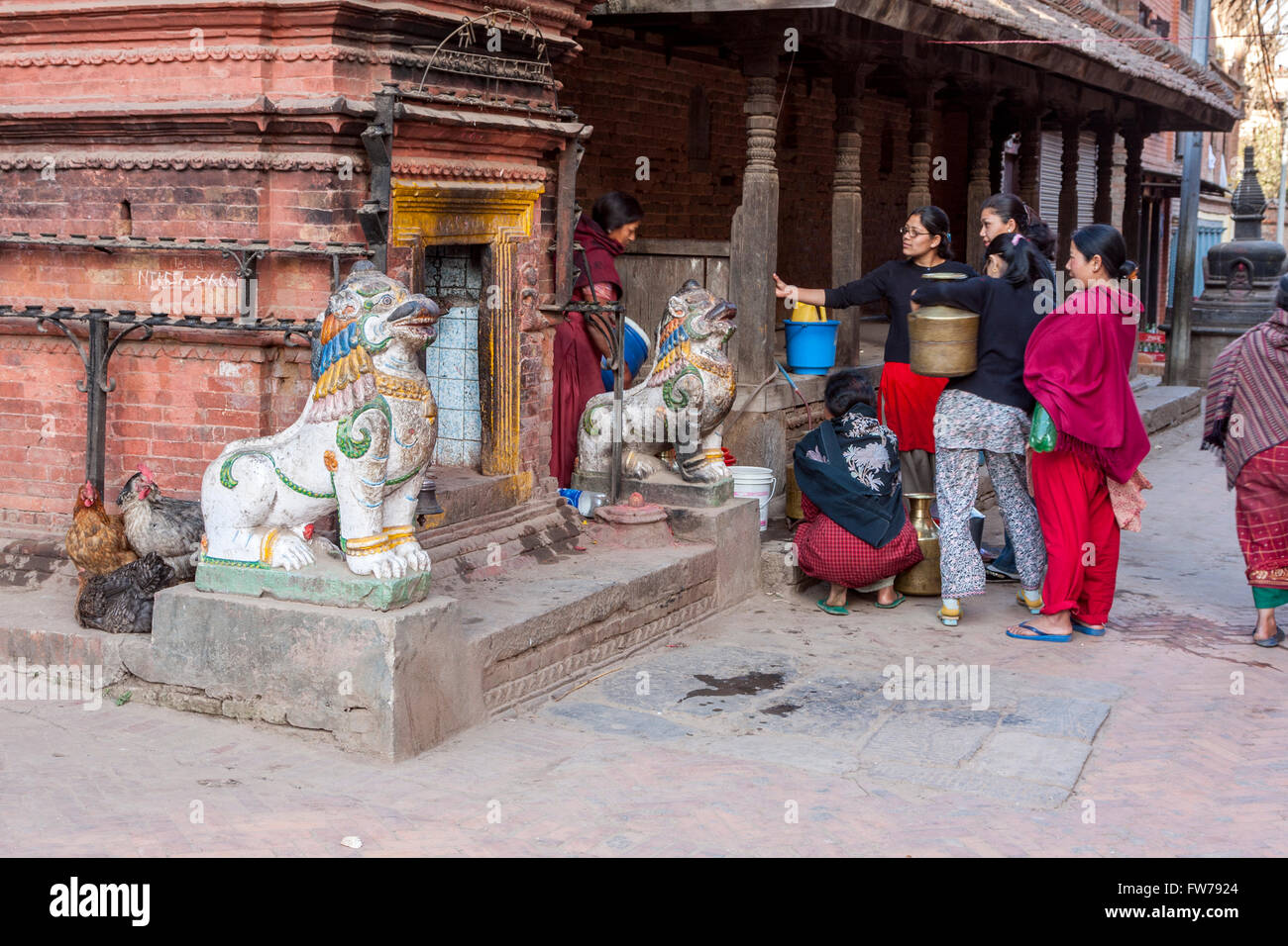 Bhaktapur, Nepal.  Frauen warten ihrerseits an die öffentliche Wasserversorgung tippen.  Löwen bewachen einen Nachbarschaft Hindu-Schrein auf linken Seite. Stockfoto