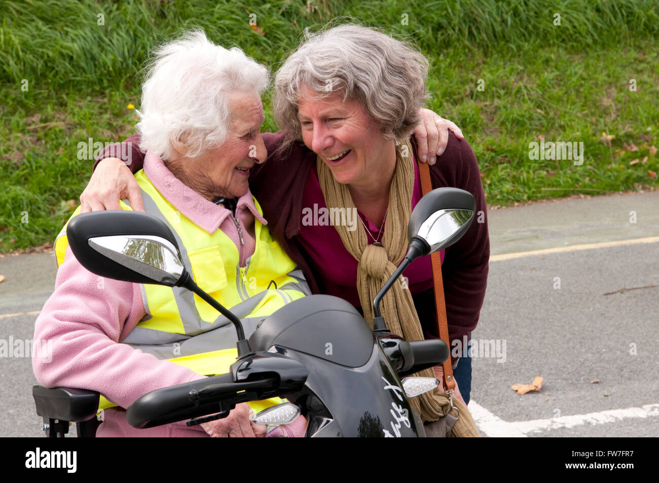 Ältere Frau sitzt in ihrem Elektromobil im Gespräch mit ihrem Betreuer Stockfoto