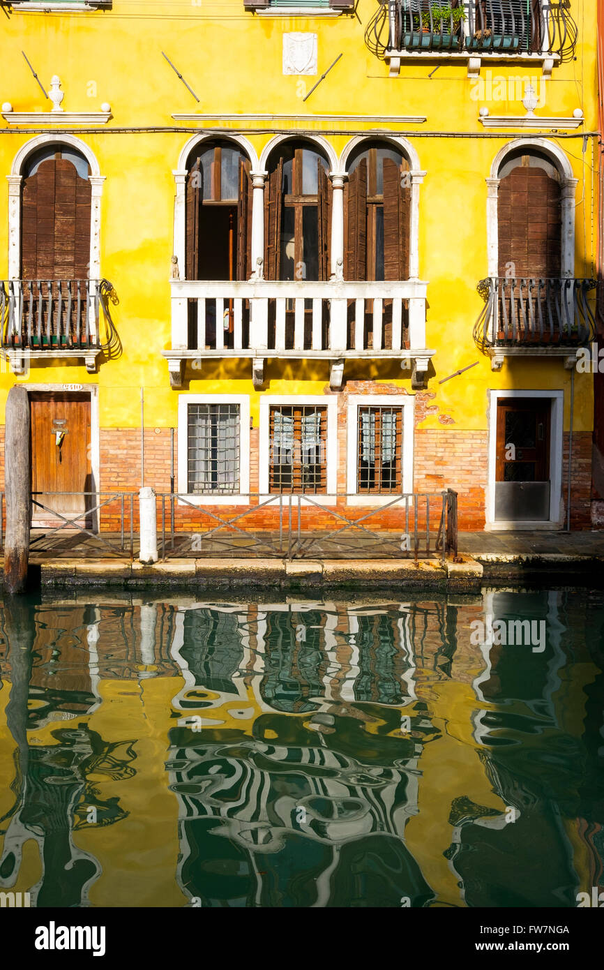 Ein gelbes Haus wirft seine Reflexionen auf einem Kanal in Venedig. Stockfoto