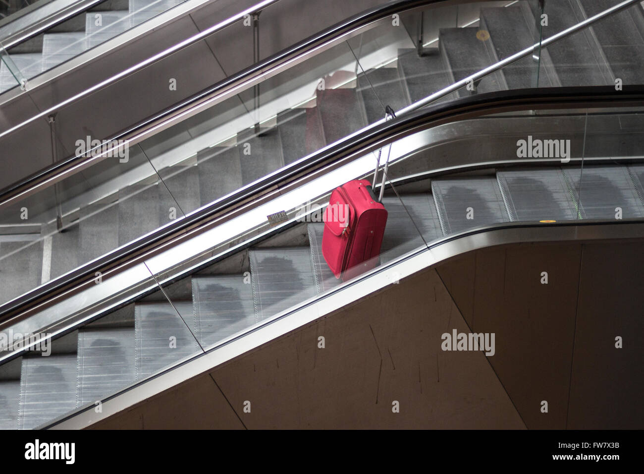 roten rollenden Koffer auf Rolltreppe alleine reisen Stockfoto