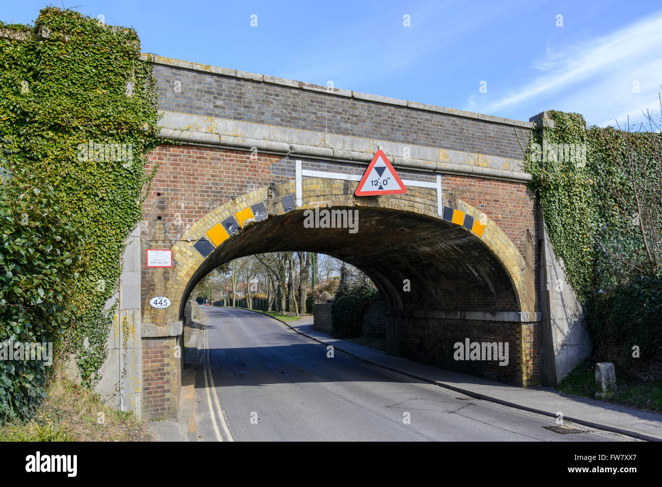 Ziegel-Eisenbahnbrücke mit Höhe Beschränkung Zeichen über eine Straße in England, UK. Stockfoto