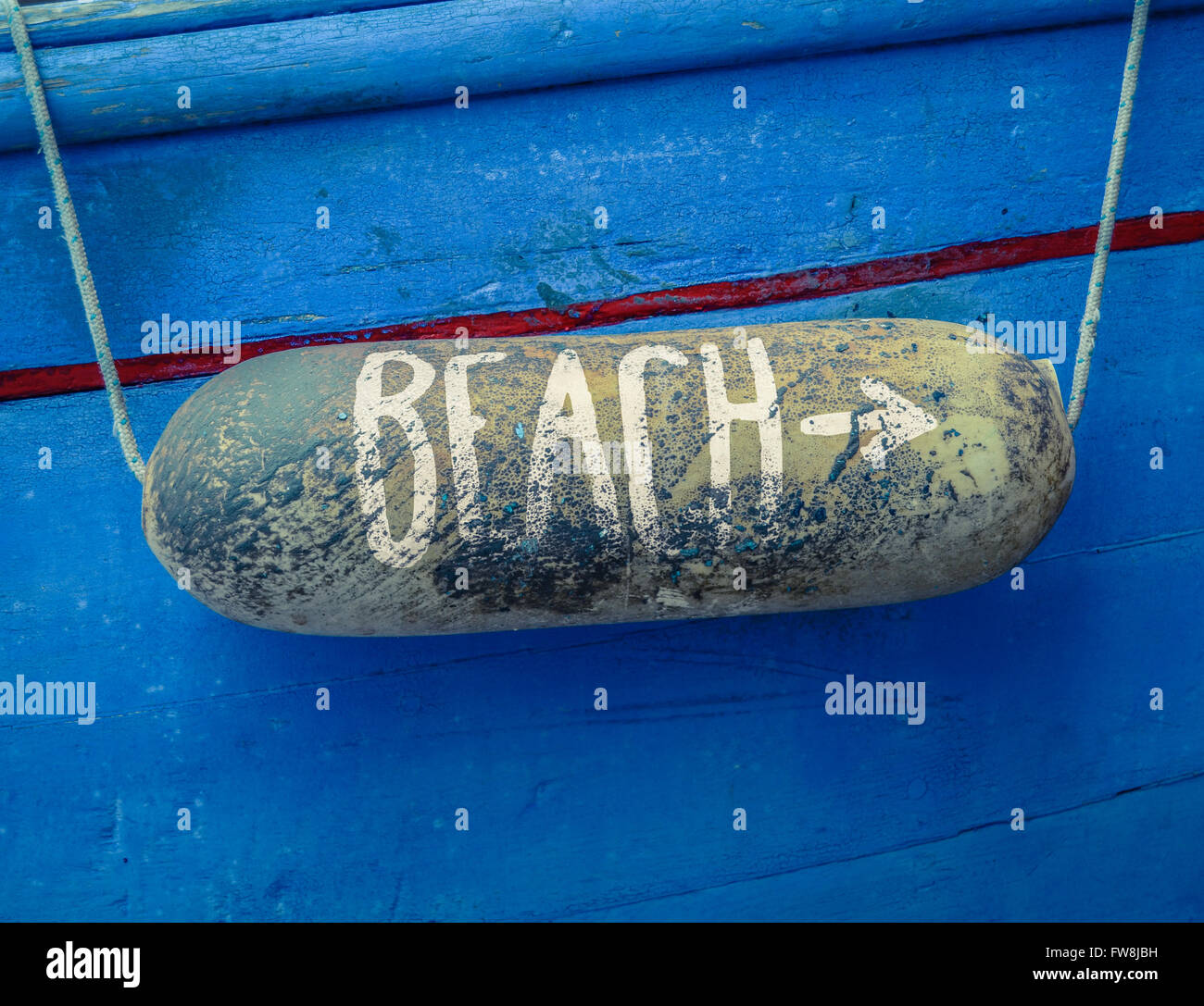 Rustikale Zeichen für einen Strand auf einer Boje auf der ein altes blaues Boot Stockfoto