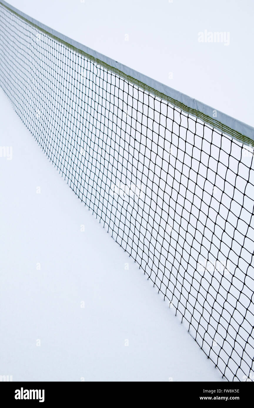 Abstrakte Muster, die durch das Netz auf einem Tennisplatz, wo ein schweren Sturz des Schnees die Spielfläche in einer dicken Schicht aus weißem Schnee bedeckt hat scheint es in dem Surrouding Schnee verschwinden und wieder erscheinen, wo sie schwarz gefärbt ist. Stockfoto