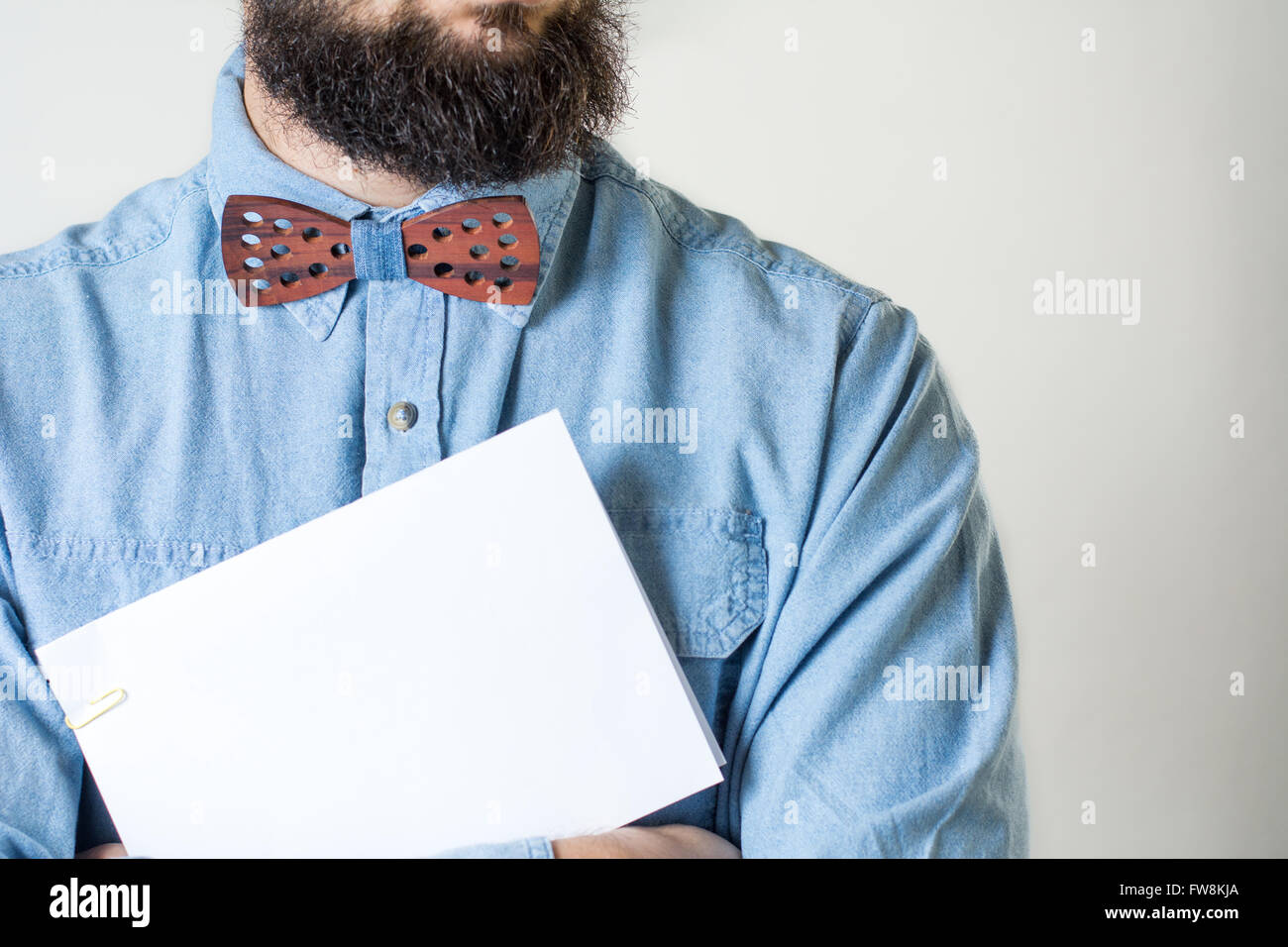 Bärtiger Mann mit einer hölzernen Fliege hält ein weißes Blatt Papier Stockfoto