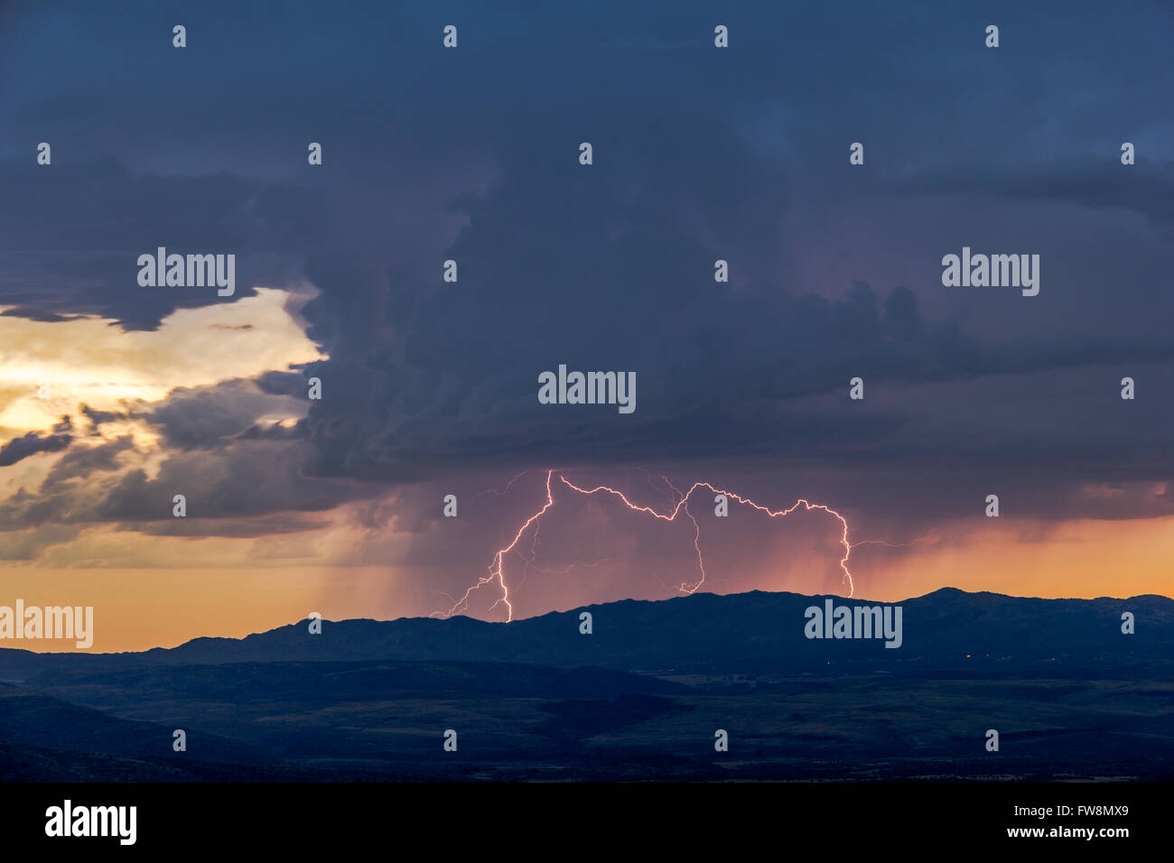 Entfernter Blitz von Wolke zu Boden über einem Berg während eines Gewitters bei Sonnenuntergang Stockfoto
