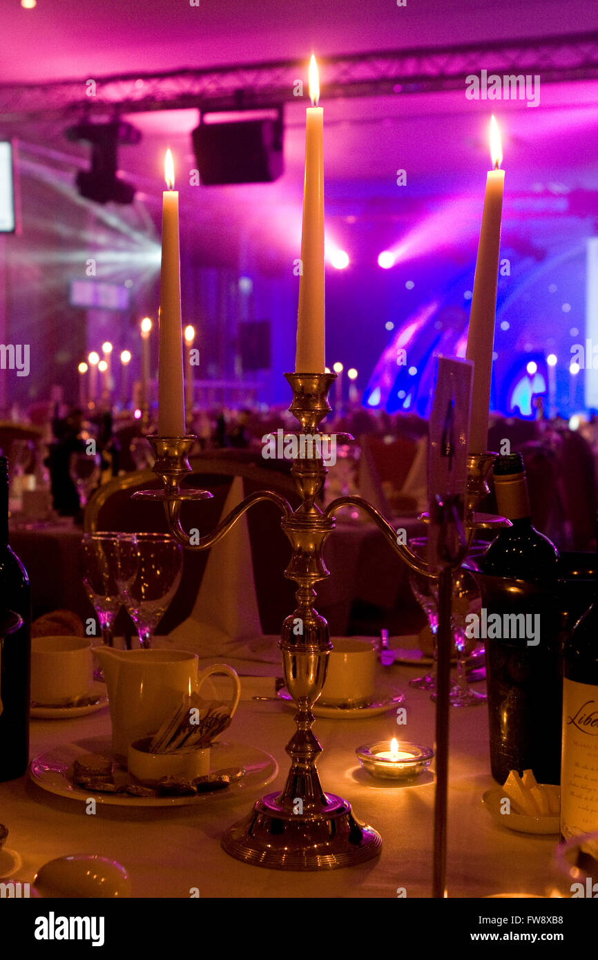 Ein Speisesaal in einem großen Hotel, das für eine corporate Abendveranstaltung ausstaffiert, stimmungsvolle Beleuchtung Komplimente ist der Essbereich, wo Tische mit Kerzen und auch eine Bühne aufgestellt sind, beleuchtet in leuchtenden Farben am anderen Ende des Raumes. Stockfoto