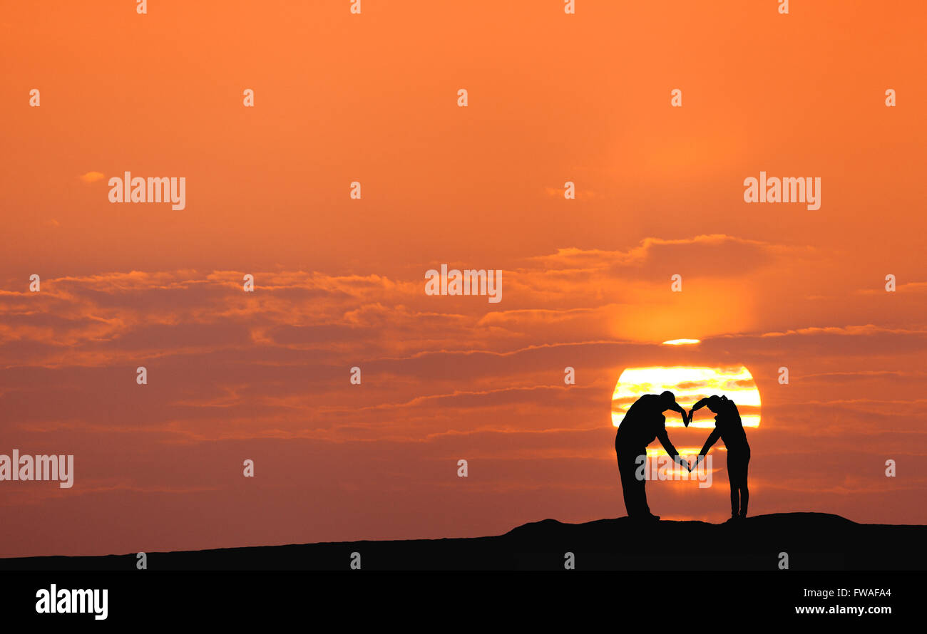 Sonnenuntergang Landschaft mit Silhouette von Mann und Frau, die Hand in Hand gegen die Sonne und bunten Himmel auf dem Hügel in s in Herzform Stockfoto
