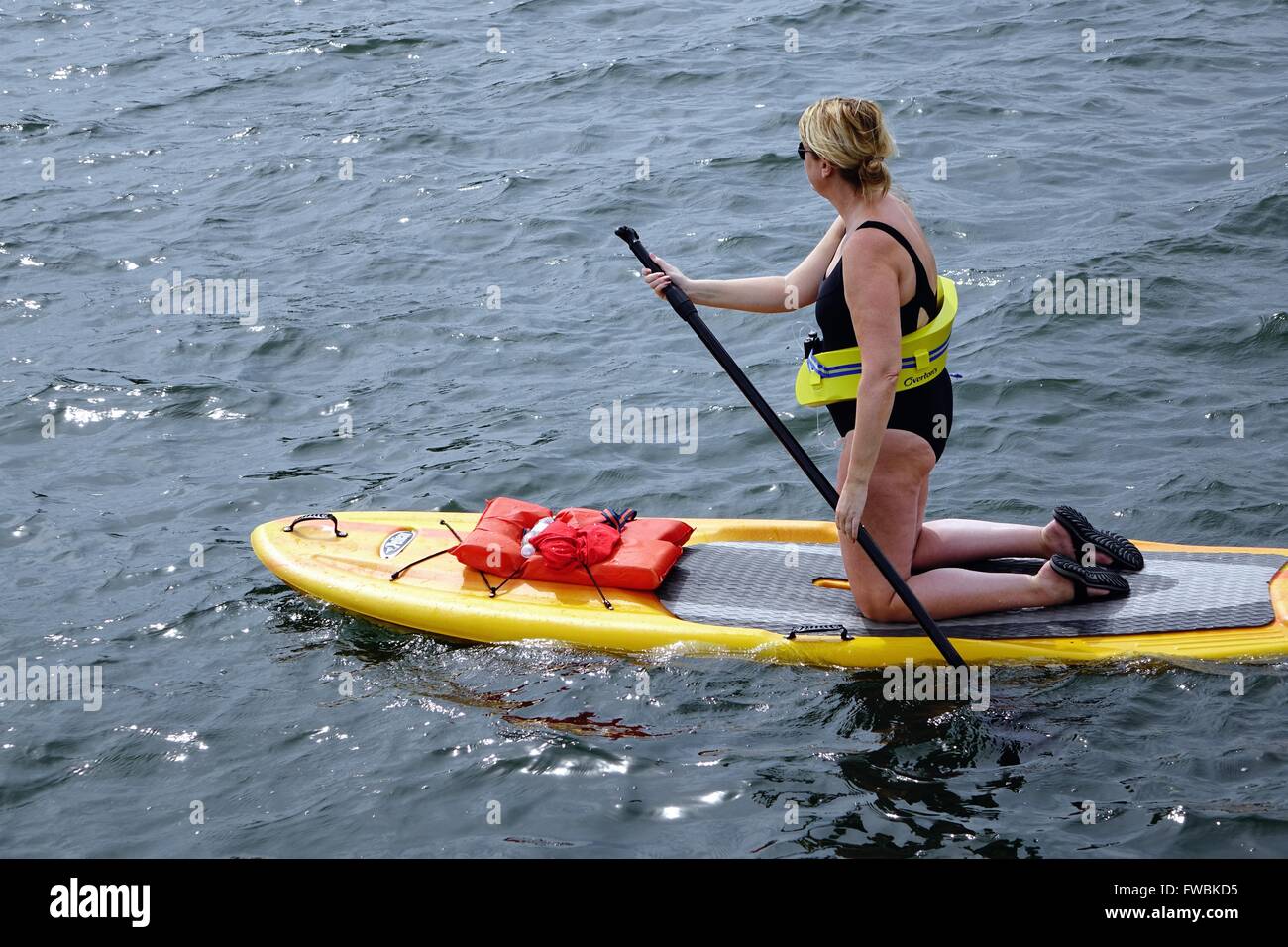 Paddleboarder auf Knien tragen Schwimmhilfe auf Taille Stockfoto