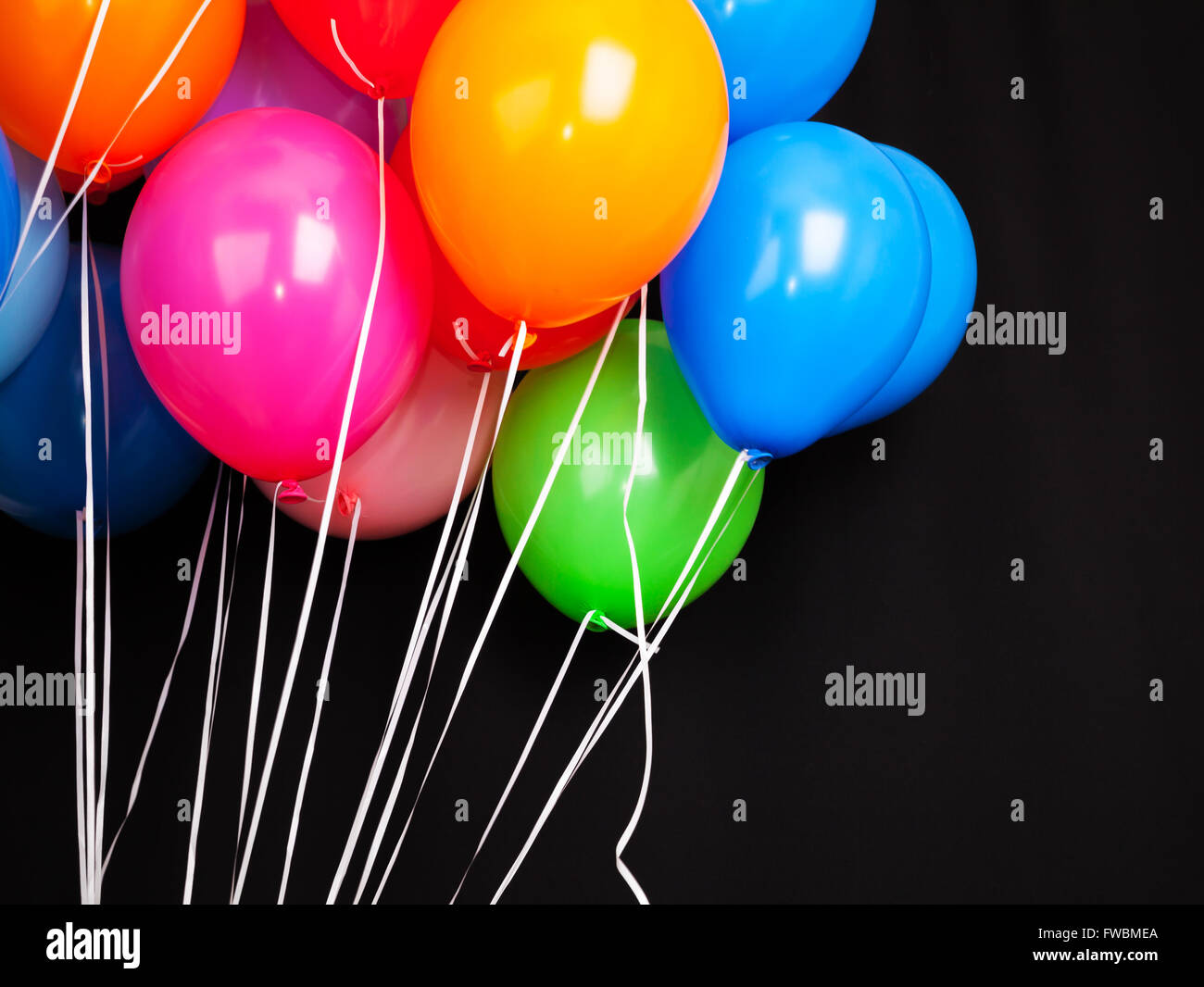 Gruppe von bunten Luftballons auf Bändern auf schwarzem Hintergrund Stockfoto