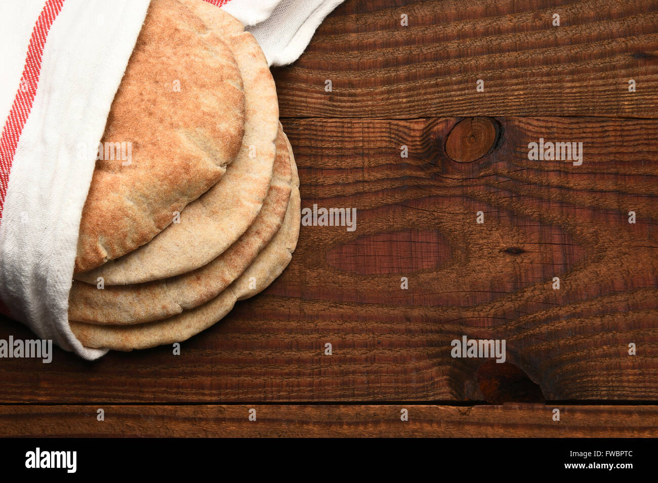 Vollkorn Fladenbrot auf einem rustikalen Holztisch mit Textfreiraum. Das Brot ist in ein Handtuch gewickelt und von einem hohen Winkel gesehen. Stockfoto