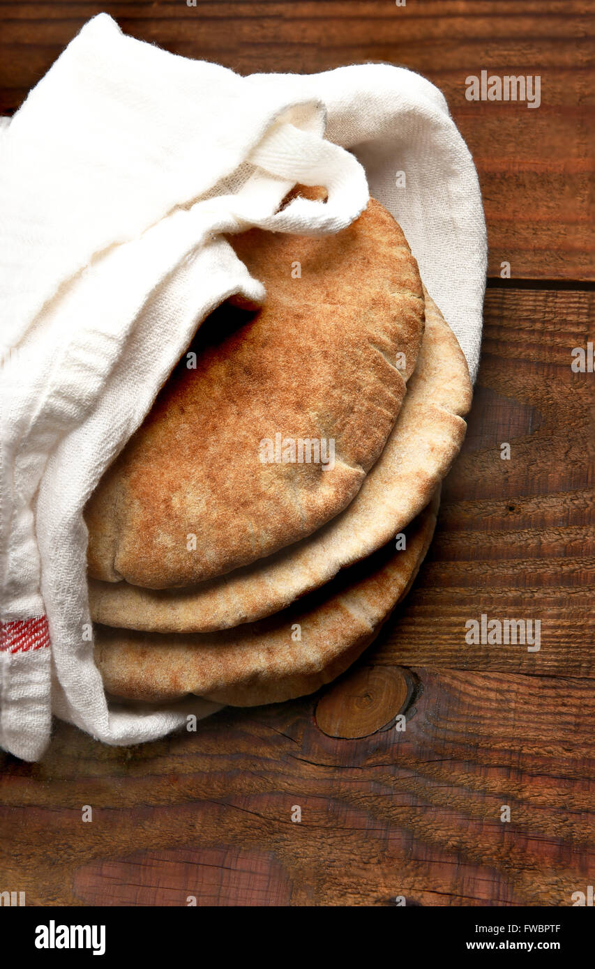 Vollkorn Fladenbrot auf einem rustikalen Holztisch mit Textfreiraum. Das Brot ist in ein Handtuch gewickelt und von einem hohen Winkel gesehen. Verti Stockfoto