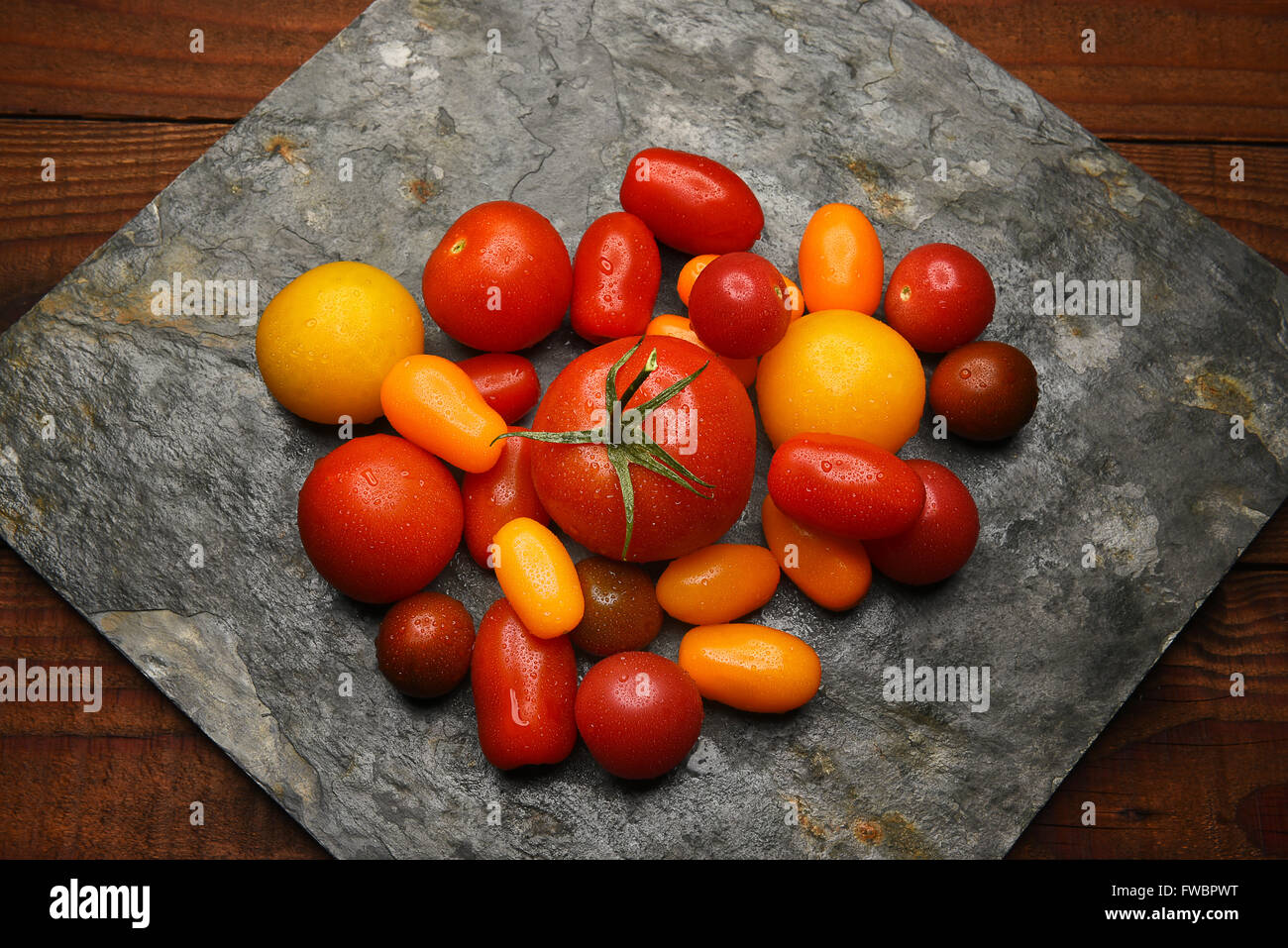 Draufsicht auf eine Gruppe von Medley Tomaten auf eine Platte aus Schiefer auf rustikale Oberfläche des Holzes. Stockfoto